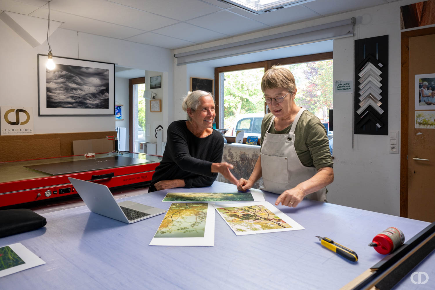 Claire et une artiste devant une table avec des oeuvres imprimées
